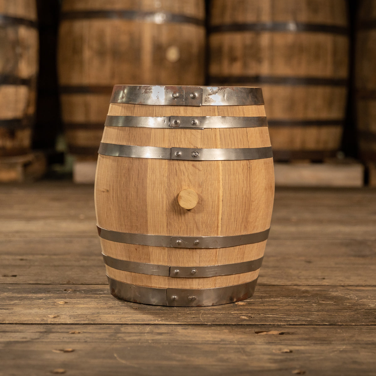 Brand new 5 gallon white oak barrel with shiny steel rings and clean staves with large barrels in the background