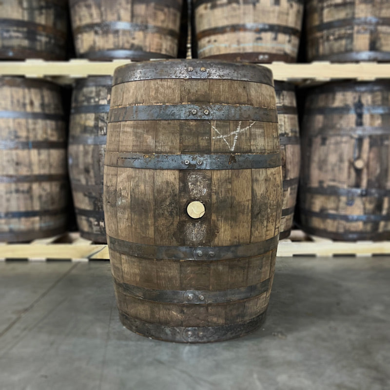 Bunghole side of a Cincoro Añejo Tequila Barrel (Ex-Whiskey) with other used tequila barrels stacked on pallets in the background