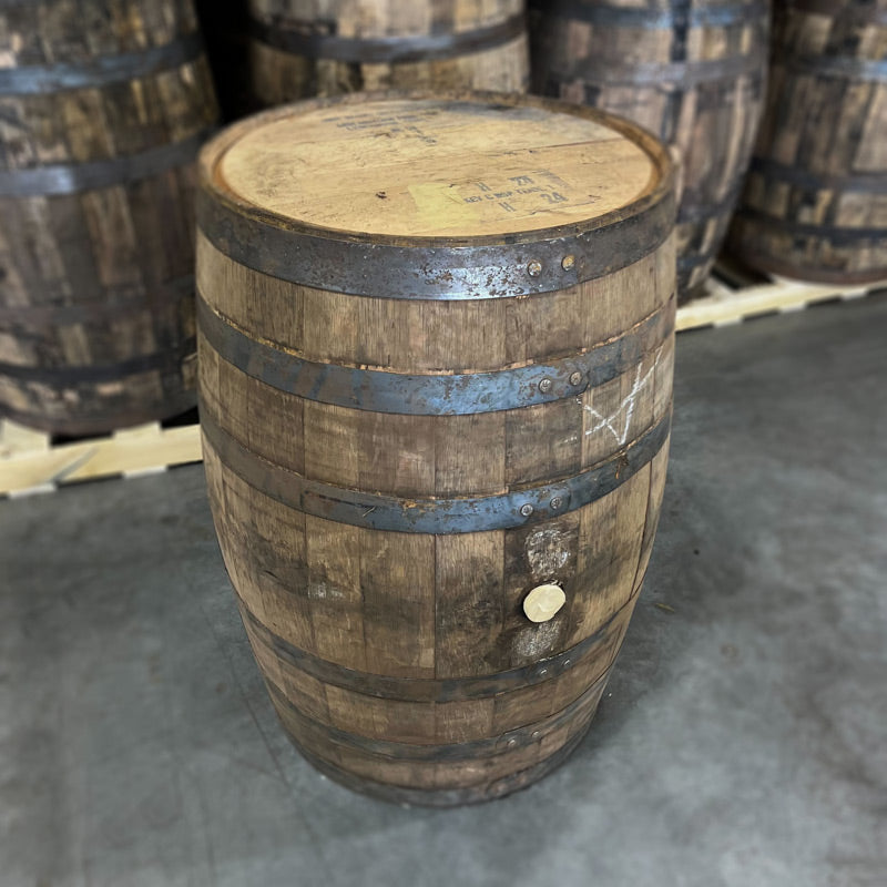 Head and bunghole side of a Cincoro Añejo Tequila Barrel ex-whiskey with Jack Daniel's distillery markings on the head with other used tequila barrels in the background
