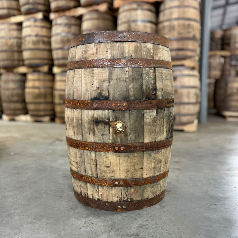 Side of a Booker's Bourbon Barrel with rusted bands and other used bourbon barrels stacked on pallets in the background