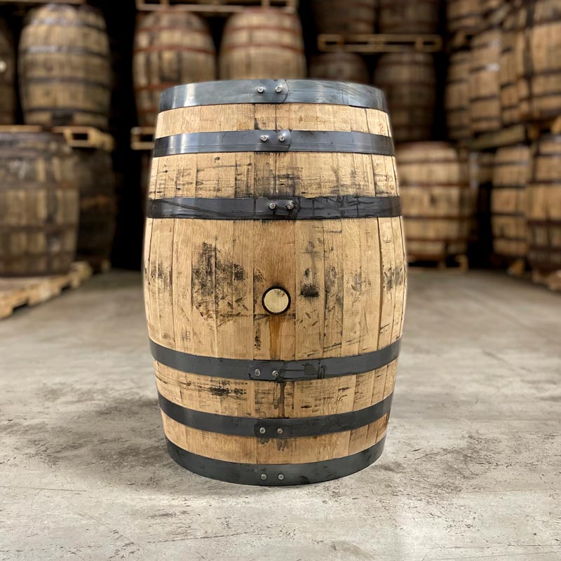 Side of an Old Forester 1910 Bourbon Whisky barrel with other used bourbon barrels stacked on pallets in the background