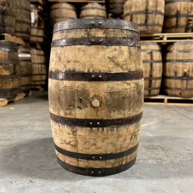 Side of a Lucky Seven Bourbon Holiday Toast Barrel with other used bourbon barrels stacked on pallets in the background