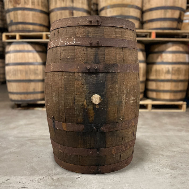 Side of a Head of a Bardstown Bourbon Plantation Rum Cask Finish Barrel with other used barrels stacked on pallets in the background