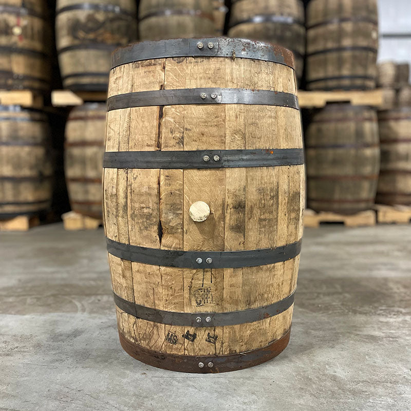 Side of a Straight Edge Bourbon barrel with other used bourbon and whiskey barrels stacked on pallets in the background