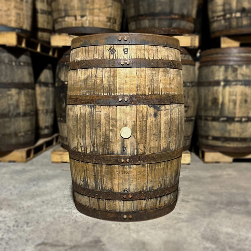Side with bung hole of a Western Spirits Bourbon Barrel with other used bourbon barrels in the background
