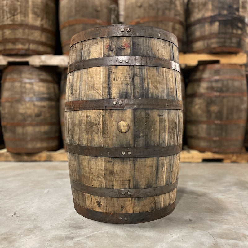 Side with bung of a Wild Turkey Rye Whiskey Barrel with other used whiskey barrels stacked on pallets in the background