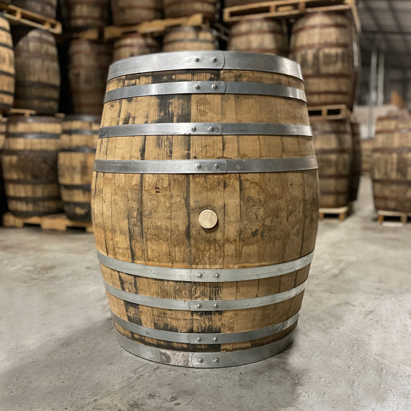 Side with bung of an Old Elk Armagnac Cask Finished Bourbon Barrel with other used barrels stacked on pallets in the background