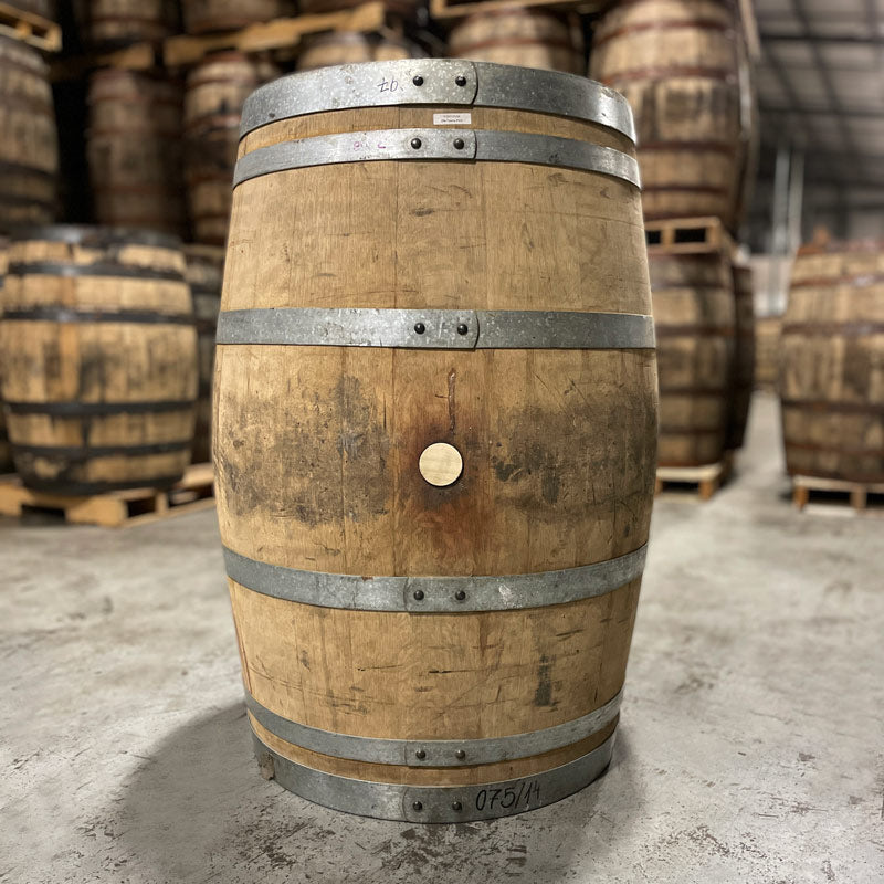 Side with bung of an Old Elk Port Cask Finish Bourbon Barrel with other used barrels stacked on pallets in the background