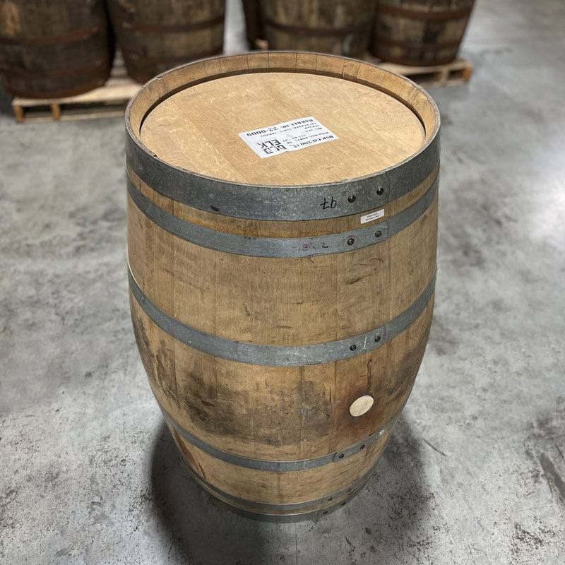 Head and side with bung of an Old Elk Port Cask Finish Bourbon Barrel with other used barrels on pallets in the background