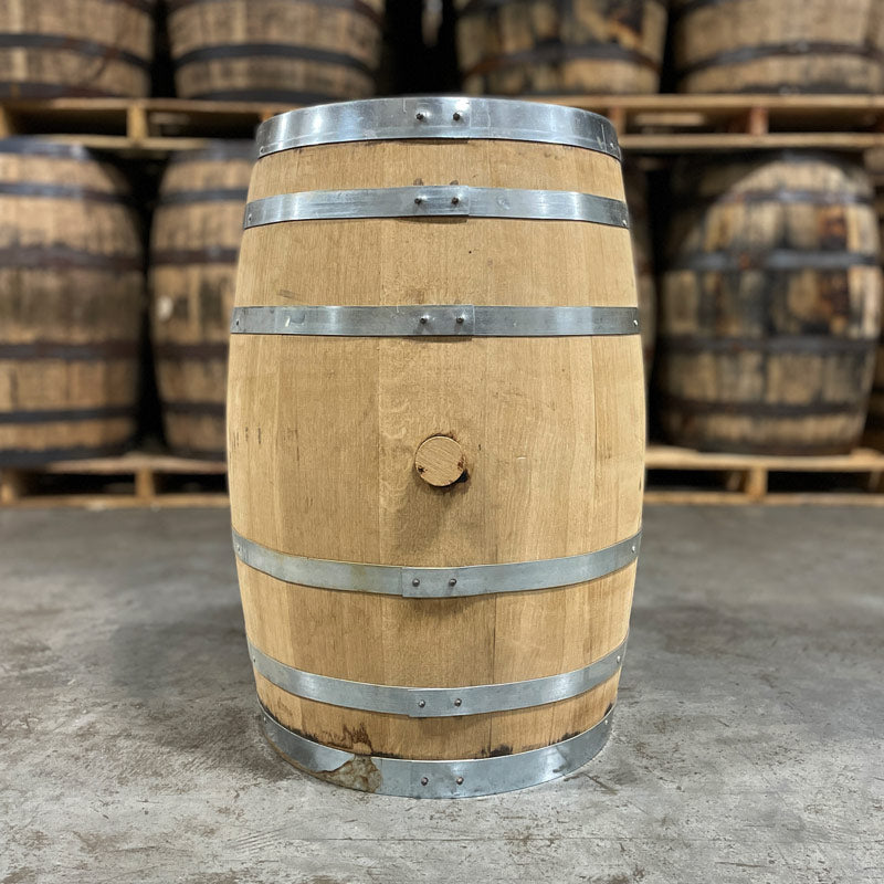 Side view with bung of a 30 Gallon Lonely Oak Bourbon Barrel with other used whiskey barrels on stacked on pallets in the background