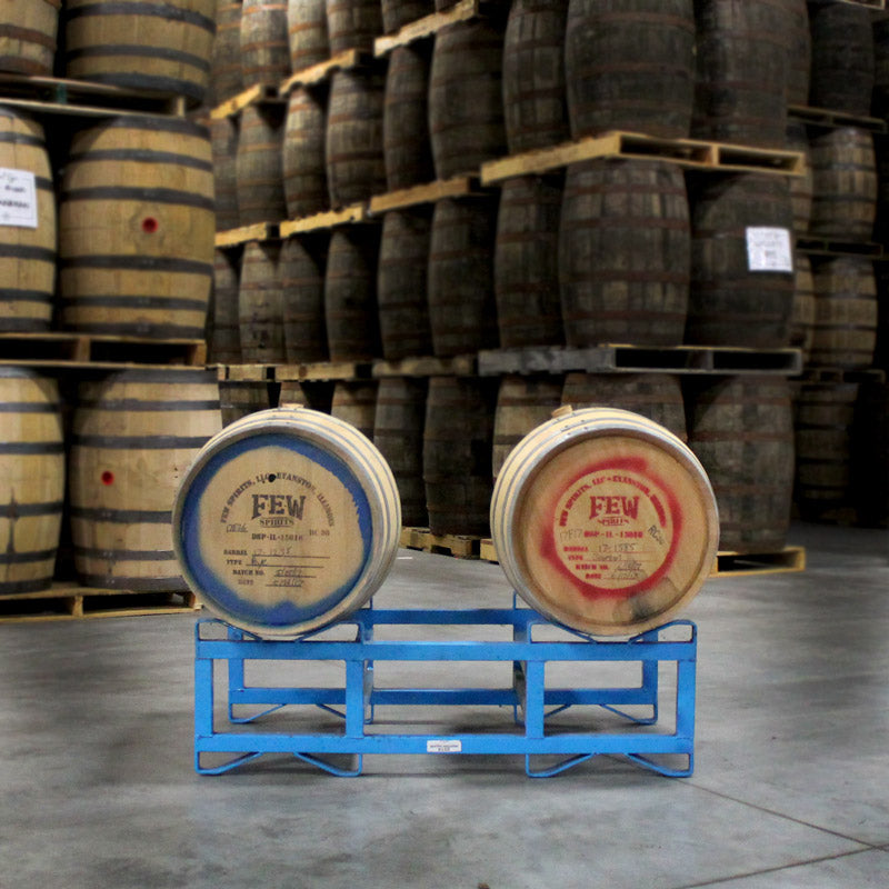 A FEW Spirits Rye Whiskey and a FEW Spirits Bourbon barrel with distillery logos and text on heads sitting on a barrel rack with barrels stacked on pallets in background