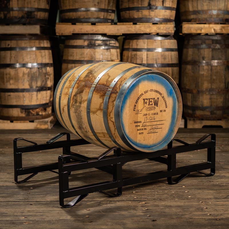 30 gallon FEW Spirits Rye Whiskey barrel on a rack with larger barrels stacked on pallets in the background