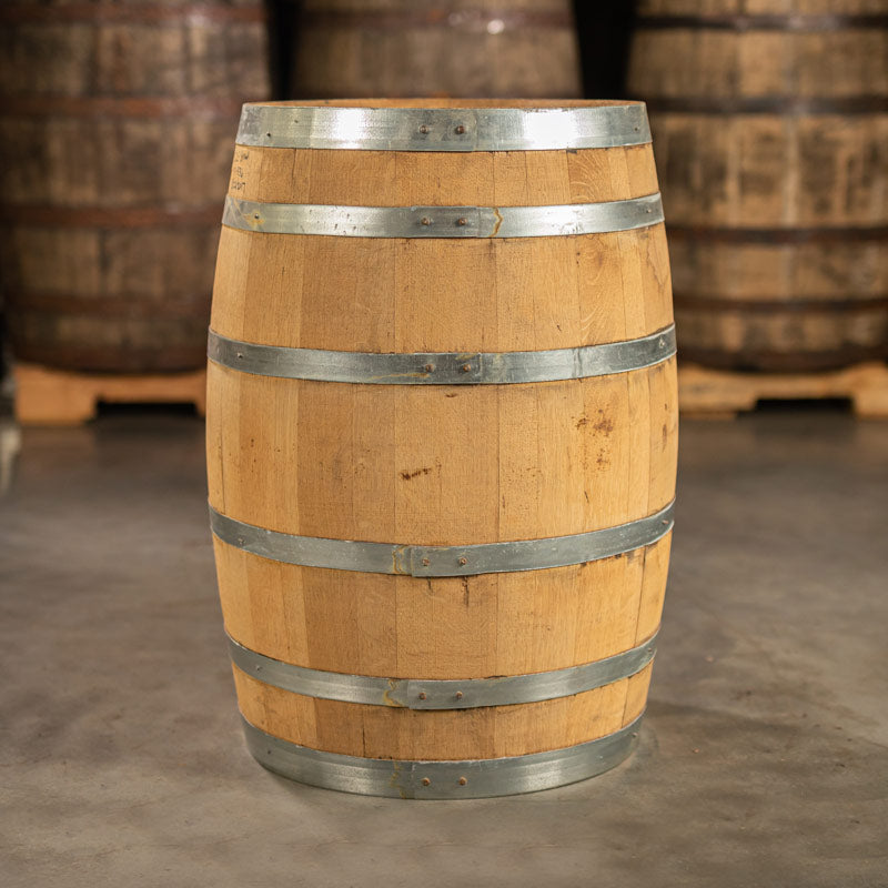 Side of a 30 Gallon Old Line Spirits Single Malt Whiskey Barrel with shiny, steel rings and other used whiskey barrels on pallets in the background