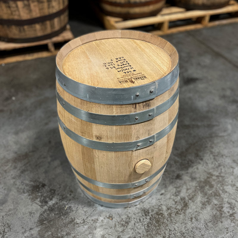 Head with handwritten notes and side with bung of a 10 Gallon Lonely Oak Bourbon Barrel with other used barrels on pallets in the background
