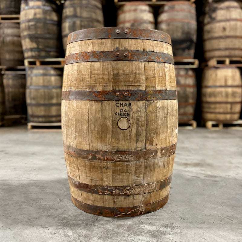 Side of a Castle & Key Bourbon Barrel with Char #4 stamped above the bunghole and other used bourbon barrels stacked on pallets in the background