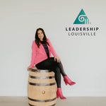 Midwest Barrel Co. Co-Founder & CEO Jess Loseke sitting on a barrel with the Leadership Louisville triangle logo in the background