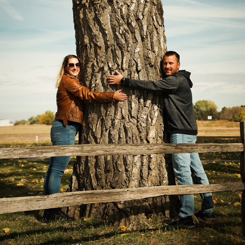 Midwest Barrel Co. co-owners Ben and Jess Loseke hug an American White Oak tree in a field near a wooden fence