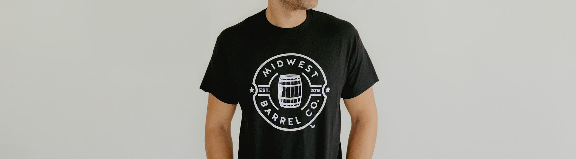 Man wearing black shirt with white Midwest Barrel Co. circle logo with Est. 2015 around a bourbon barrel in the middle of the circle