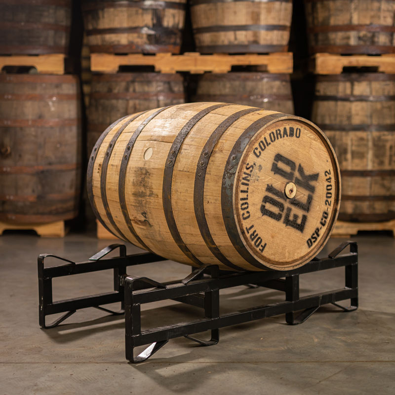 Used Old Elk bourbon barrel with head and side bungs laying on a steel rack