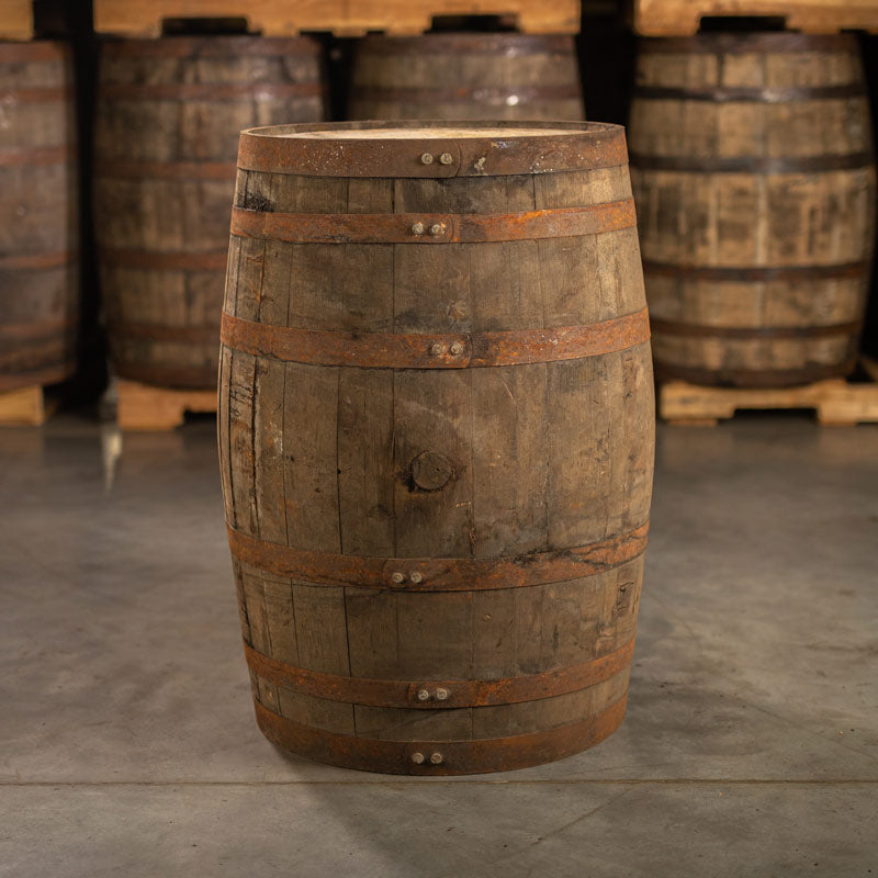 Side with bung of an 8+ Year Willett Distillery Bourbon barrel with other used bourbon barrels in a warehouse in the background