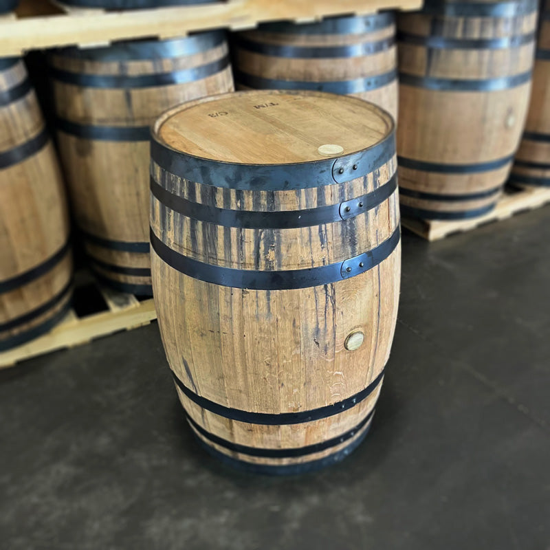 Brand new, never used American white oak whiskey barrel with belly bung side showing and other barrels on pallets in the background