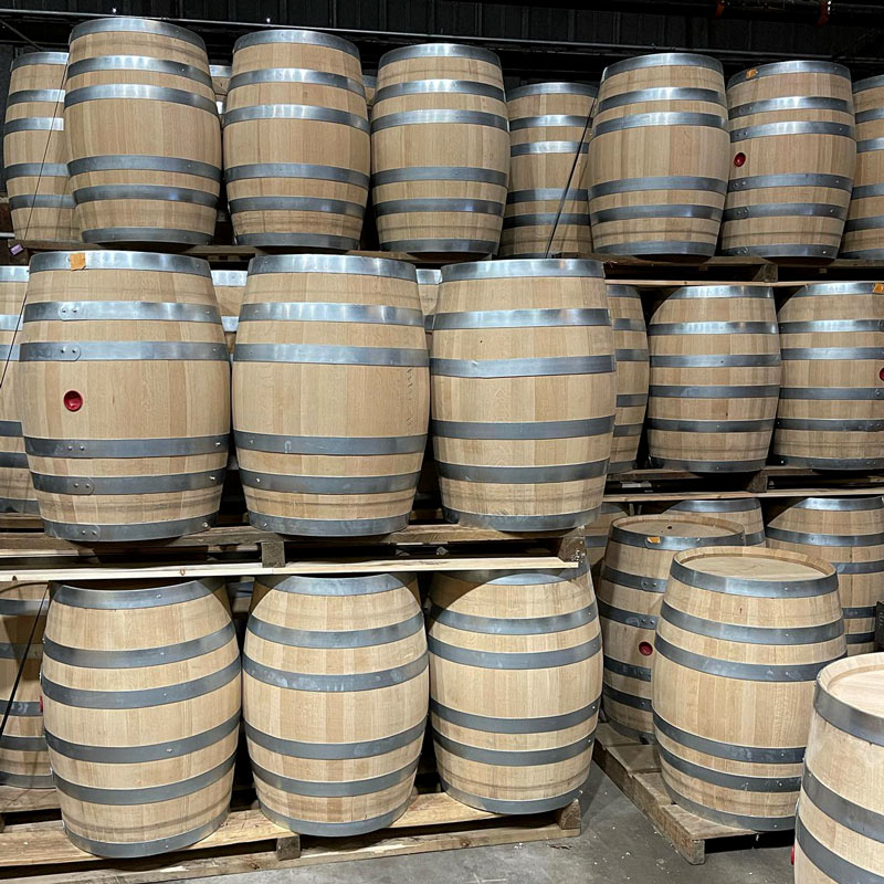 Brand new full size 53 gallon American white oak barrels for aging whiskey and bourbon stacked on pallets in a warehouse