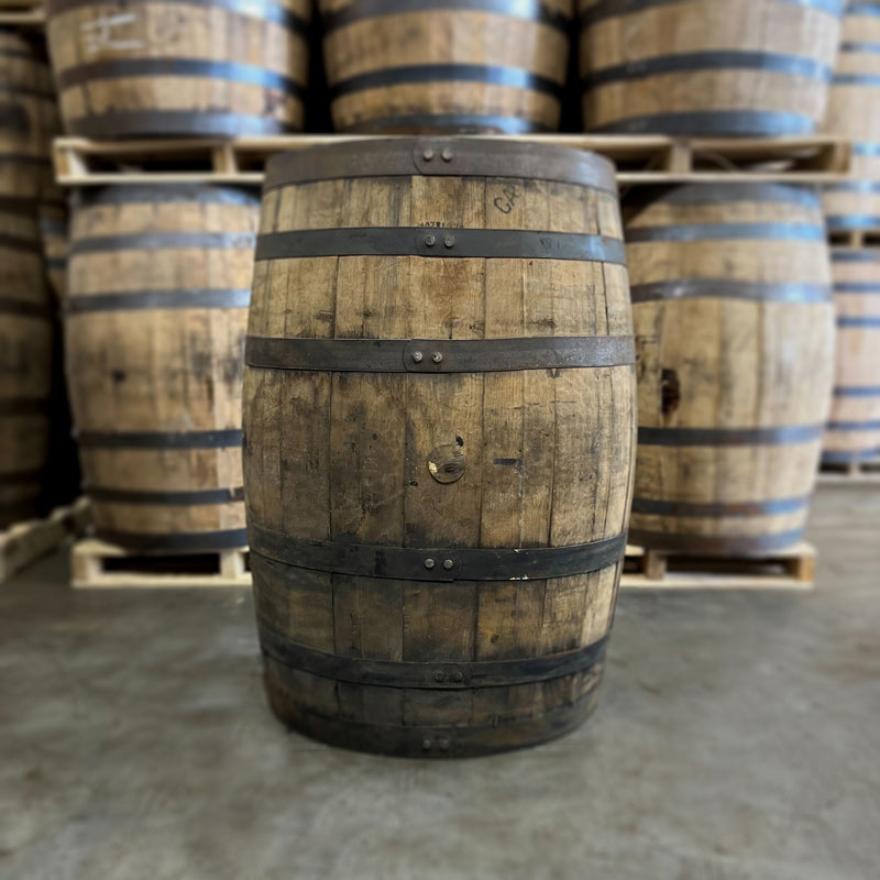 Side of an 8+ Year Jim Beam Black Extra Aged Bourbon Barrel with other used bourbon barrels stacked on pallets in the background