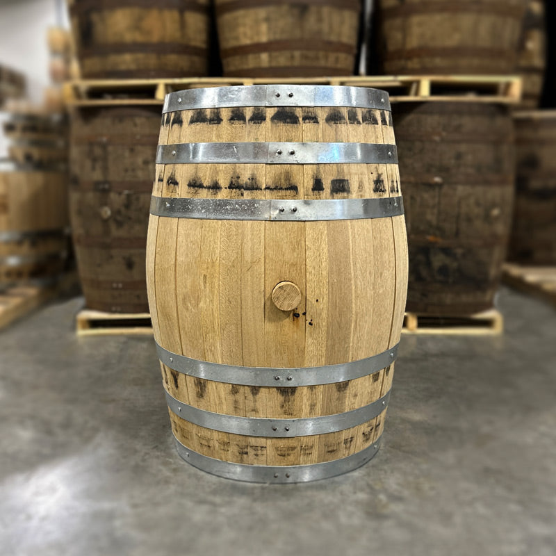 Bunghole side of a Caledonia Tom Cat Gin Barrel with other used barrels stacked on pallets in the background