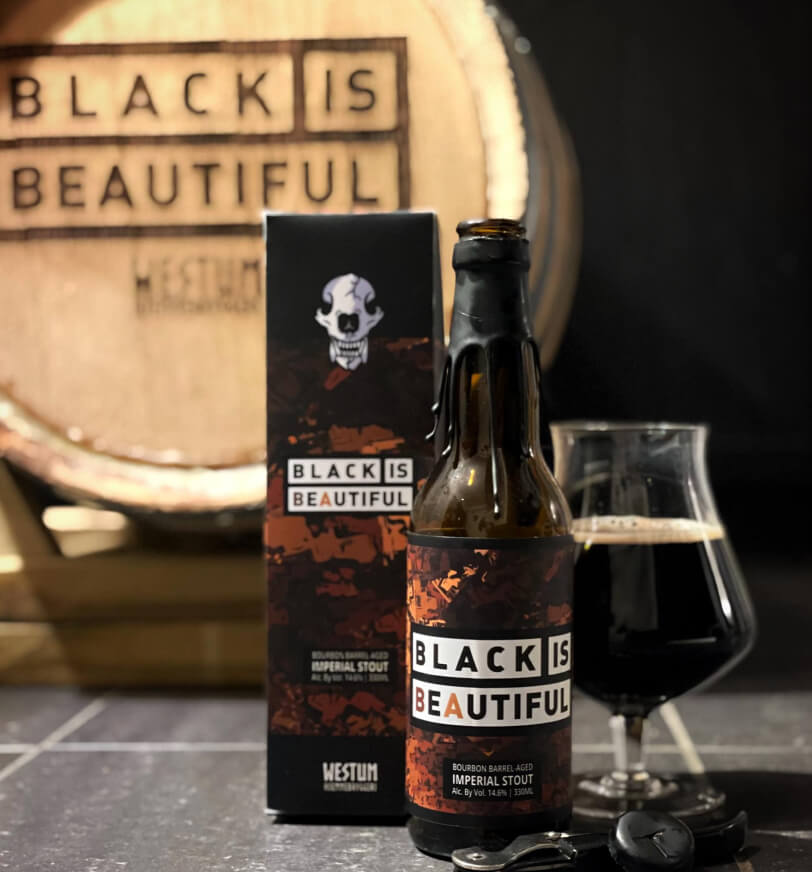 Black Is Beautiful beer box, bottle and glass with barrel in the background engraved with Black Is Beautiful logo