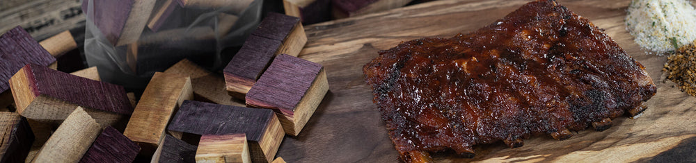 Smoked BBQ meat next to different types of barrel BBQ smoking wood chunks