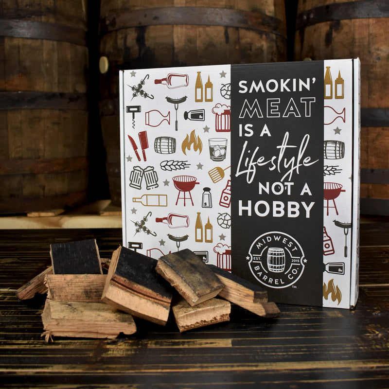 Bourbon barrel smoking wood chunks next to a holiday-themed box with Midwest Barrel Logo and text on the box that says Smoking meat is a lifestyle, not a hobby