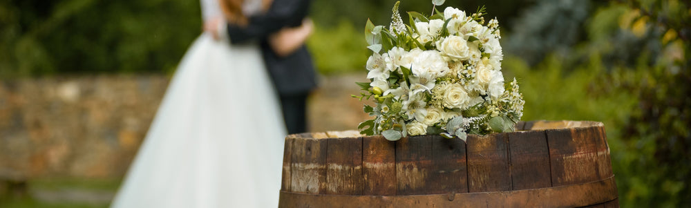 Floral arrangement on top of barrel with bride and groom in background