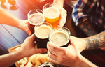 People clinking beer glasses together over a table and board with cheeses