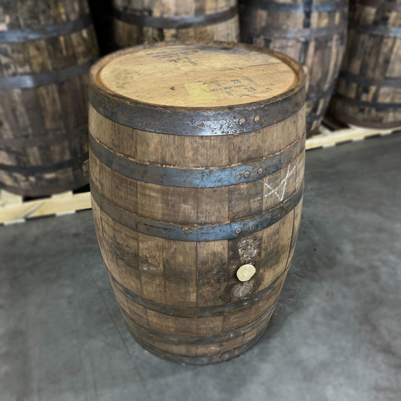
                  
                    Head and bunghole side of a Cincoro Añejo Tequila Barrel ex-whiskey with Jack Daniel's distillery markings on the head with other used tequila barrels in the background
                  
                