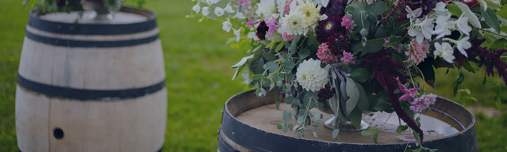 Two decor barrels with floral arrangements in vases on top
