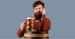 Bearded man holding large mug of beer and leaning on barrel with a thinking expression on his face and finger raised to temple