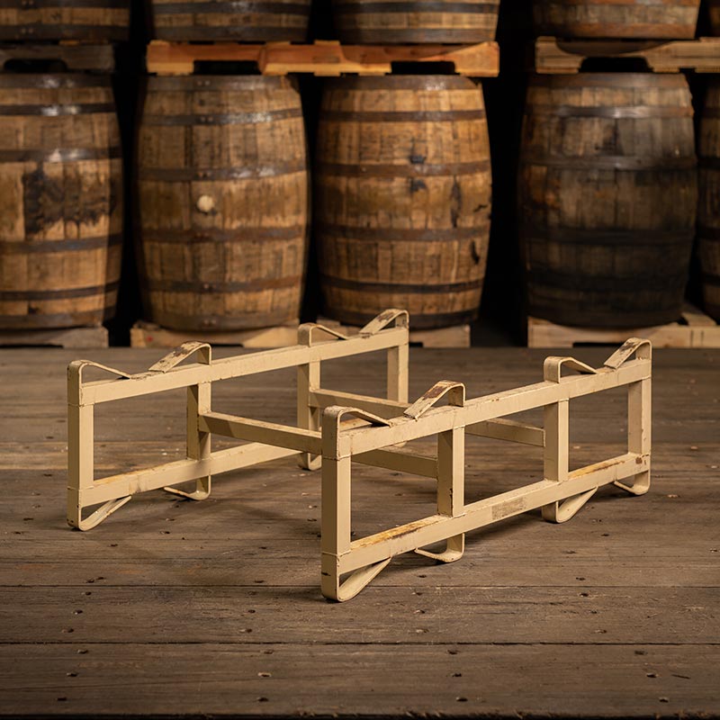 Used steel barrel rack with two single bars across in front of used bourbon barrels stacked on pallets