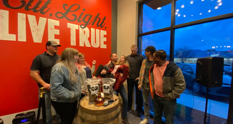 Midwest Barrel Co. employees standing behind barrel with bags of smoking chunks on top