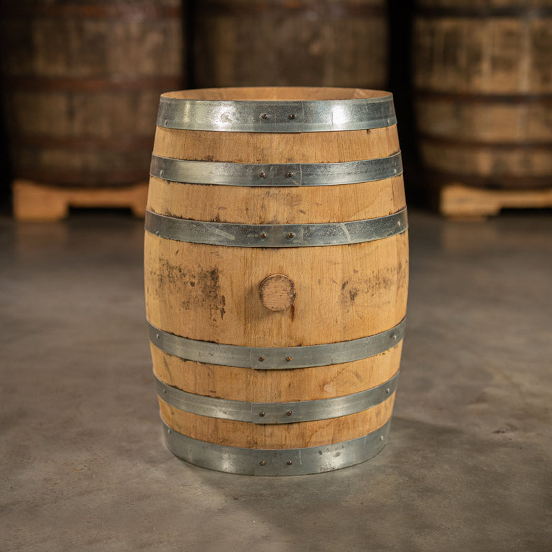 Side of a 10 Gallon Distillery 291 Bourbon Whiskey barrel with shiny, silver bands and other barrels on pallets in the background