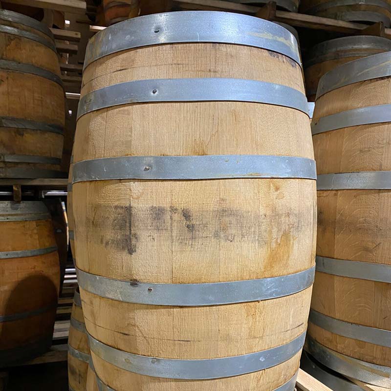 Side of a 23 Gallon Far North Spirits Rye Whiskey Barrel next to other used whiskey barrels on pallets