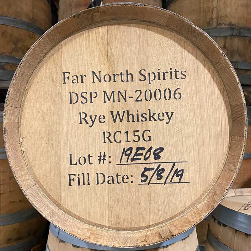Head of a 23 Gallon Far North Spirits Rye Whiskey barrel with other used whiskey barrels in the background with Far North Spirits, distillery number, fill date and other information stamped on the head