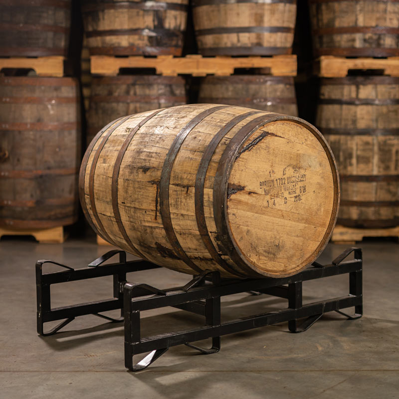 A 1792 Bourbon Barrel with Barton 1792 Distillery information stamped on the head laying on a rack with barrels stacked on pallets in the background