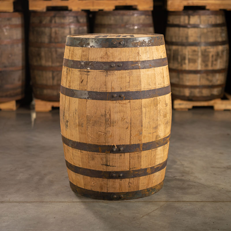 Side of an Old Elk Bourbon Barrel with a head bung and other used bourbon barrels stacked on pallets in the background