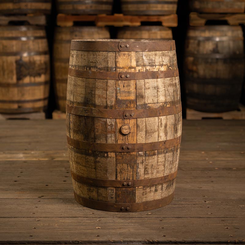 Side of a Knob Creek Bourbon barrel with other barrels in the background stacked on pallets