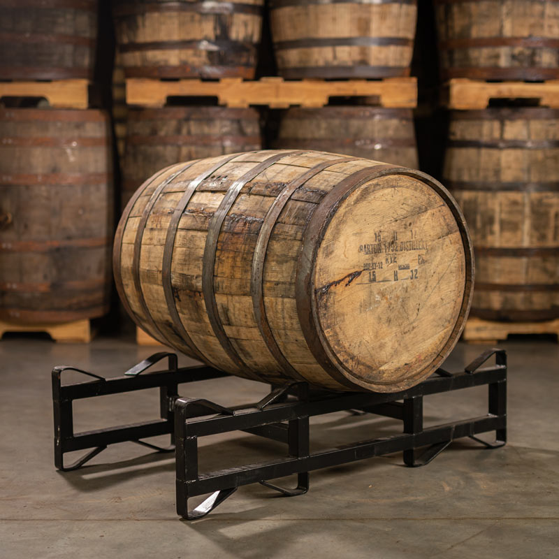 A 1792 High Rye Bourbon Barrel with Barton 1792 Distillery information stamped on the head with other barrels stacked on pallets in the background