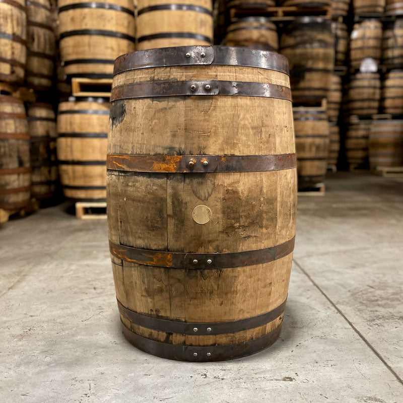 Side of an OZ Tyler Distillery Bourbon Whiskey Barrel with other used bourbon barrels stacked on pallets in the background