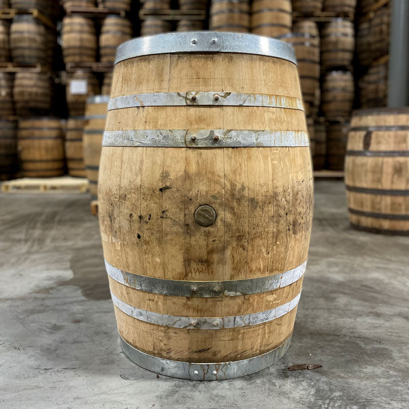 Side of a Head of a Lucky Seven Bourbon The Frenchman Cask Finish Barrel with other used barrels stacked on pallets in the background