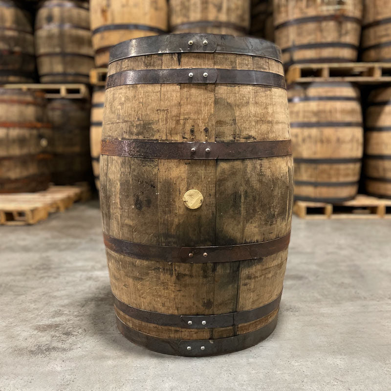 Side of a Peerless Rye Whiskey Barrel with other used whiskey barrels stacked on pallets in the background.