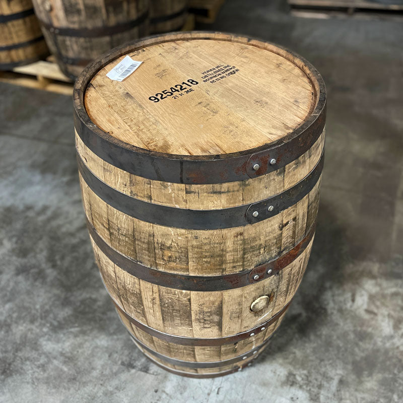 
                  
                    Head and side of a 2 year Heaven Hill bourbon barrel with distillery information stamped on the head and other used bourbon barrels in the background
                  
                