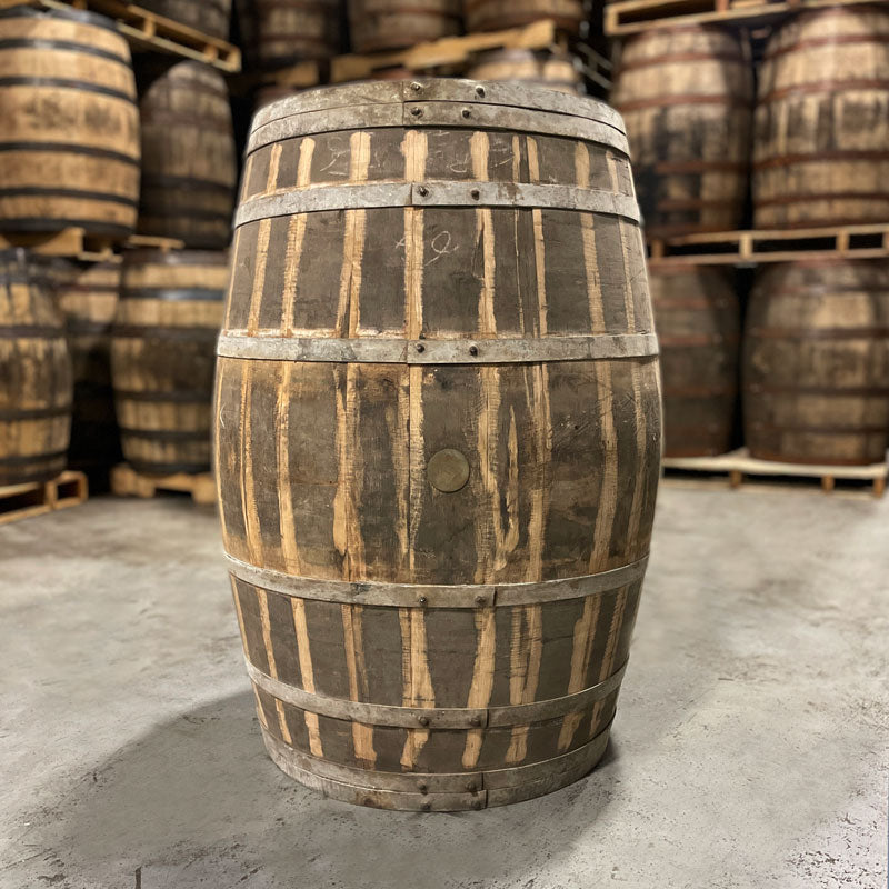 
                  
                    Side with bung of an Old Elk Cognac Finished Bourbon Barrel with other used barrels stacked on pallets in the background
                  
                